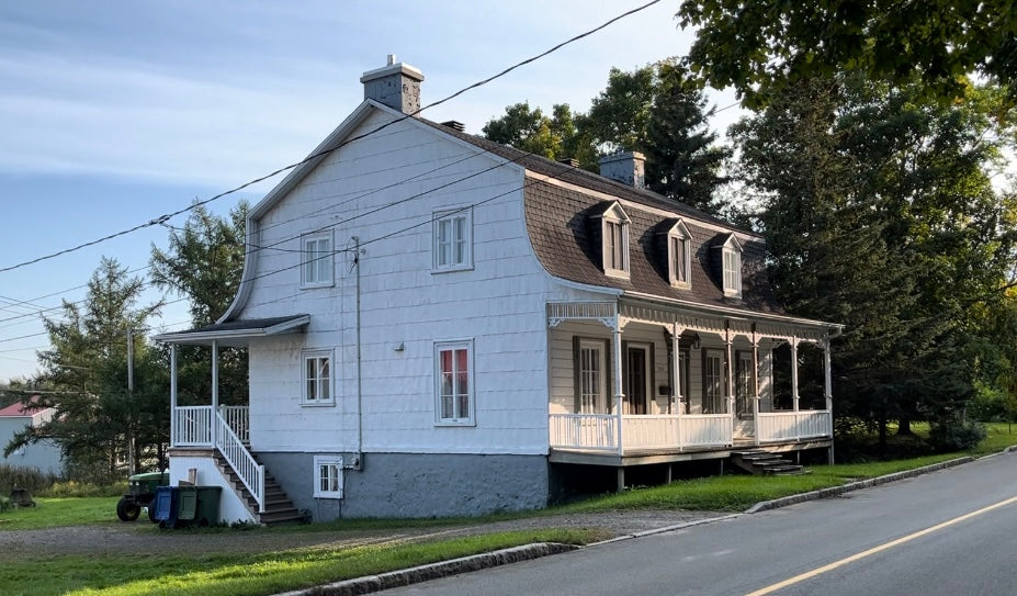 Maison ancestrale de la cidrerie Terre 50, située à l'extérieur avec un cadre naturel environnant. La maison en bois, avec son architecture traditionnelle, est entourée de verdure, mettant en valeur son charme historique et son lien avec le terroir.